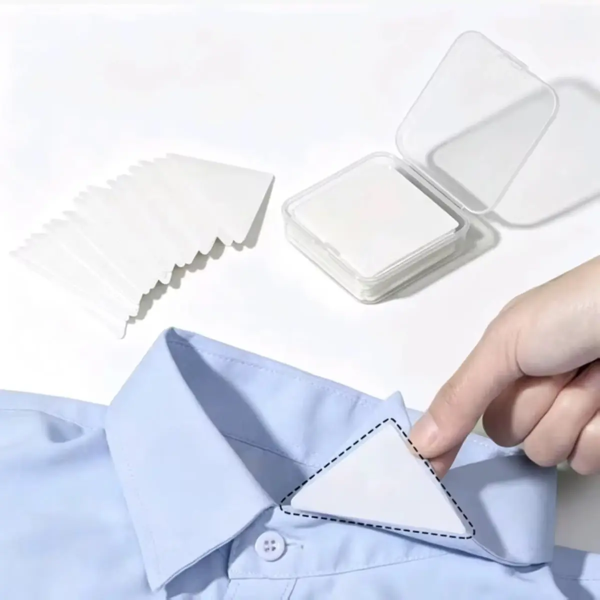 Protector adhesivo blanco para cuello de camisa, mostrado en uso sobre una prenda azul junto a una caja transparente con repuestos adicionales.