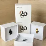 Anillos inteligentes de salud y monitoreo biométrico en cajas blancas, mostrando variantes en negro, dorado y plateado sobre fondo de madera.
