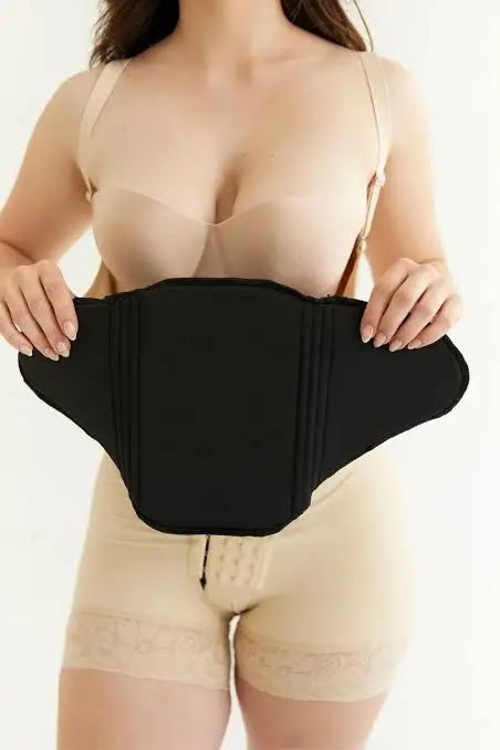Tabla abdominal moldeadora negra de diseño liso sin pliegues, sostenida por una mujer que viste faja beige, ideal para aplanado y definición de figura.