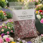 Bolsa de fertilizante para flores en pastillas de colores, ubicada en un jardín vibrante con rosas, tulipanes e hidrangeas de colores vivos.