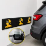 Protector de pared negro con textura de fibra de carbono y logos amarillos, junto a un auto gris para evitar golpes en la carrocería y puertas.