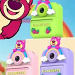 Cámara instantánea infantil con diseño de oso rosado sobre arcoíris y nubes, disponible en verde, rosado y lila con detalles de fresas.