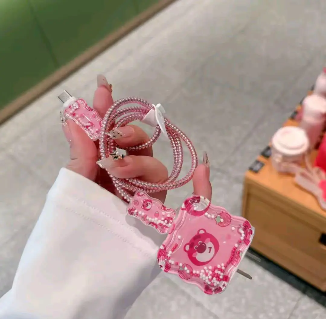 Protector de cable de silicona rosa con diseño de osito y cuentas blancas, con espiral decorativo para evitar roturas en el cargador.
