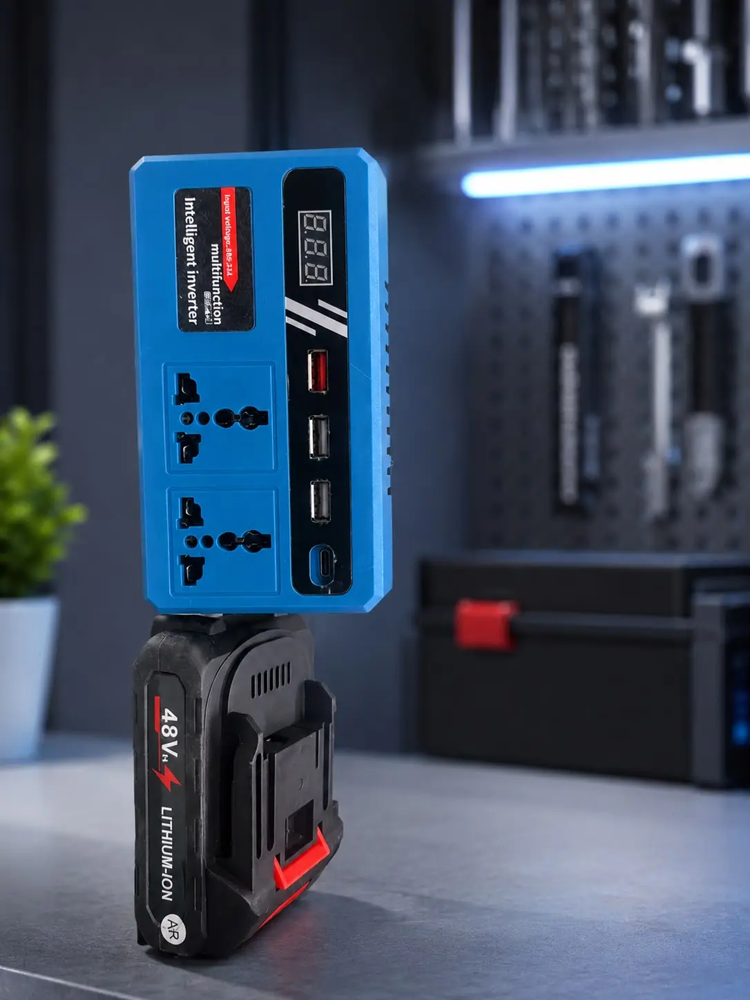 Inversor inteligente azul con pantalla digital, tomas de corriente y puertos USB, acoplado a una batería de litio de 48V en un taller.