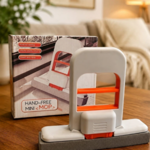Mini mopa escurridora manual blanca con detalles naranjas y esponja gris, ubicada frente a su caja de empaque sobre una mesa de madera en una sala.