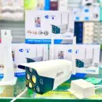 Cámara de seguridad exterior IP66 blanca con dos antenas, lentes múltiples de visión nocturna, soporte de pared y fuente de alimentación sobre fondo de cajas.