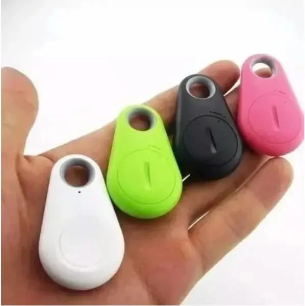 Cuatro rastreadores Bluetooth para llaves en colores blanco, verde, negro y rosa, sostenidos en la palma de una mano para mostrar su tamaño compacto.